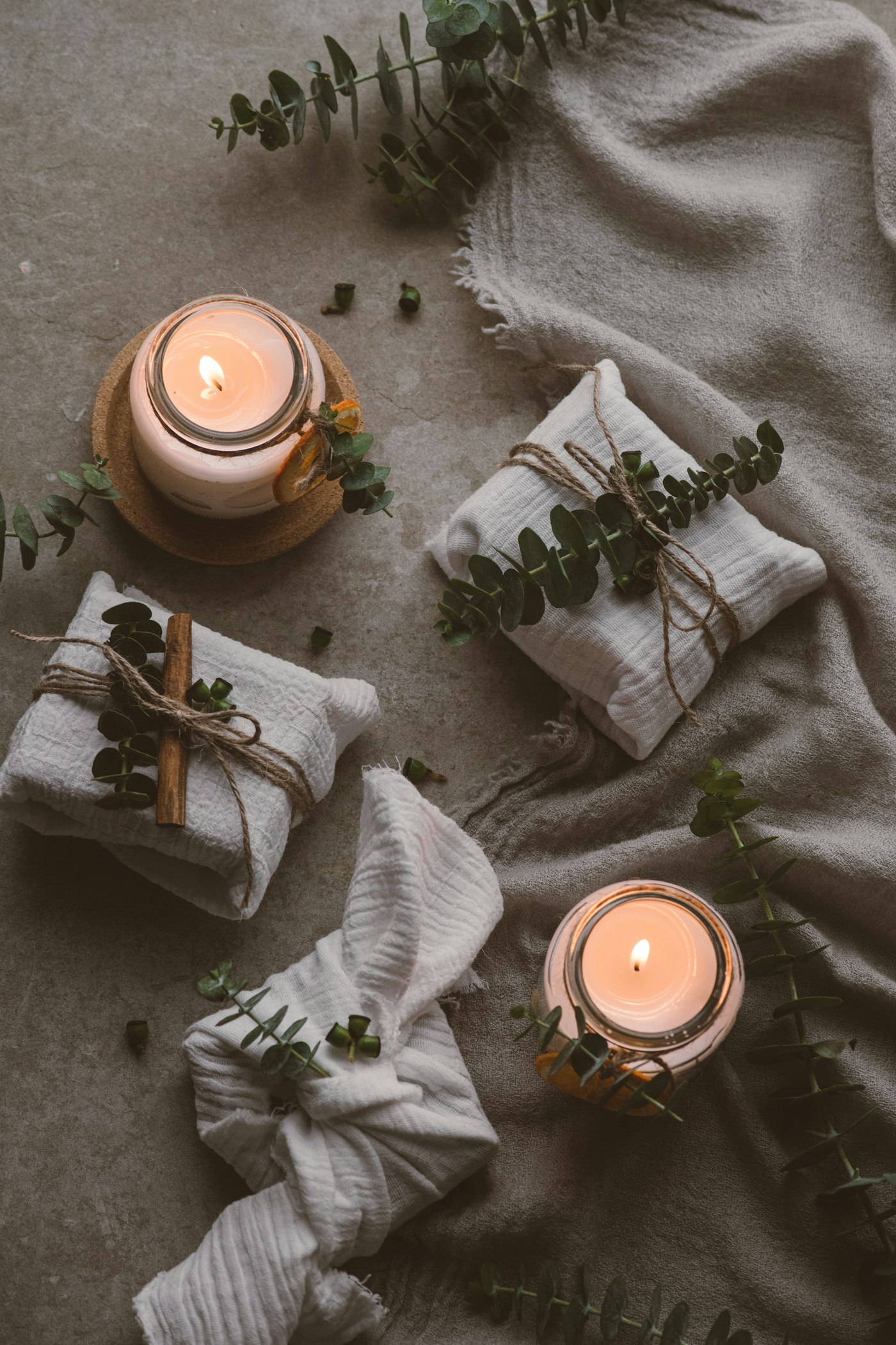 A flat lay of a candle, a wooden board, a carafe and a throw with kraft wrapping