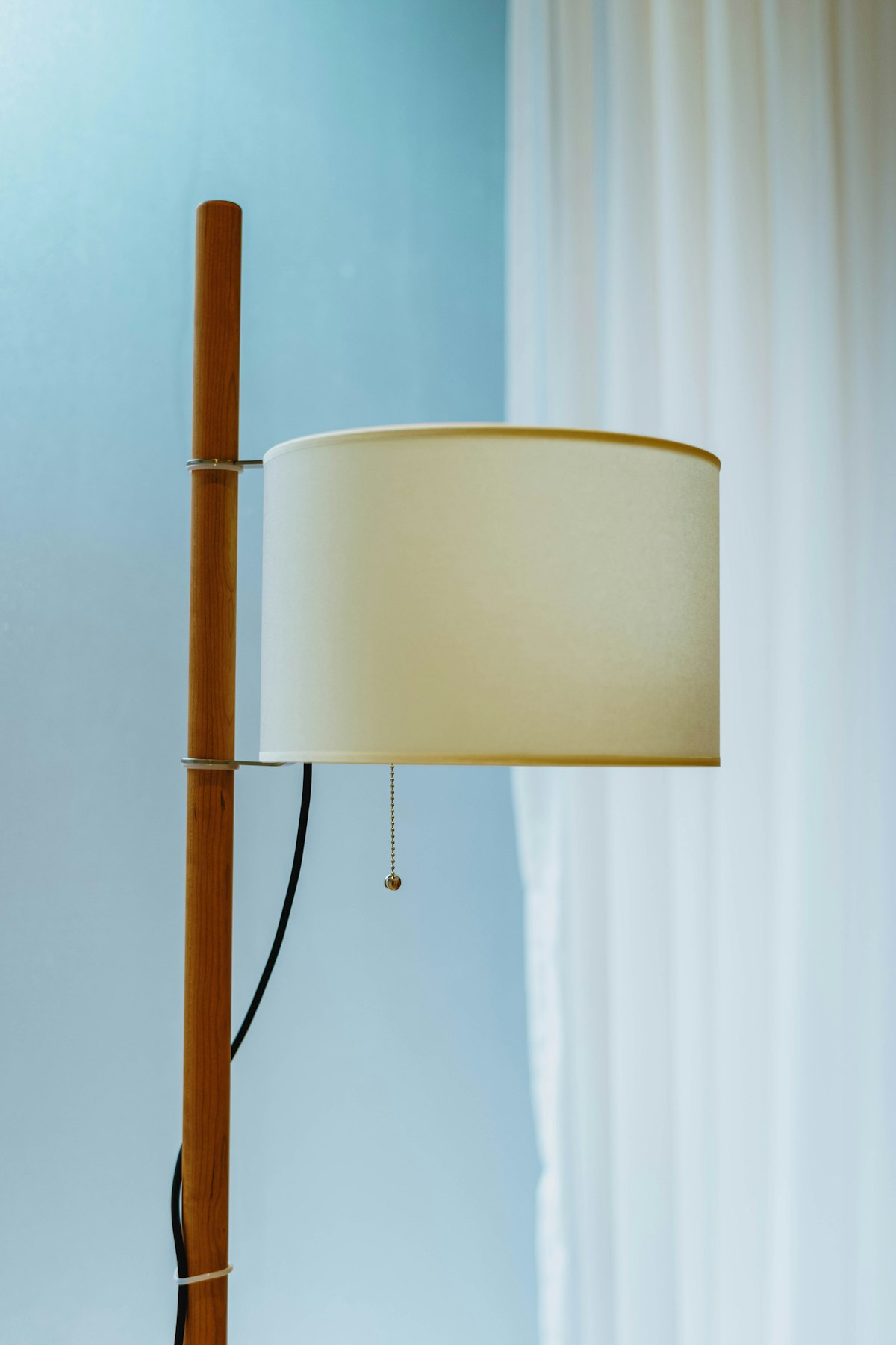 A tall floor lamp with an oak stem and a linen shade